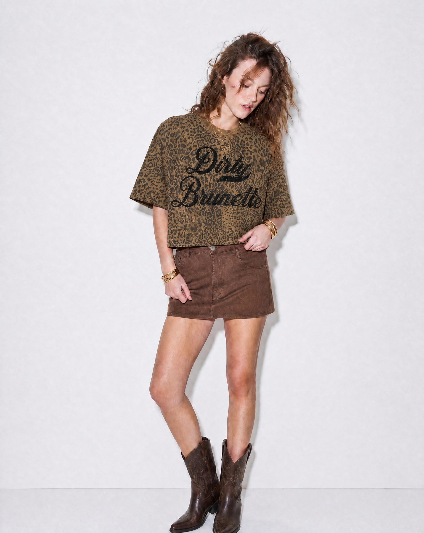 model wears a brown boxy T-shirt with an all-over animal print, contrasting ribbed crew neckline, and faded black Dirty Brunette Milkstore script graphic across the front.