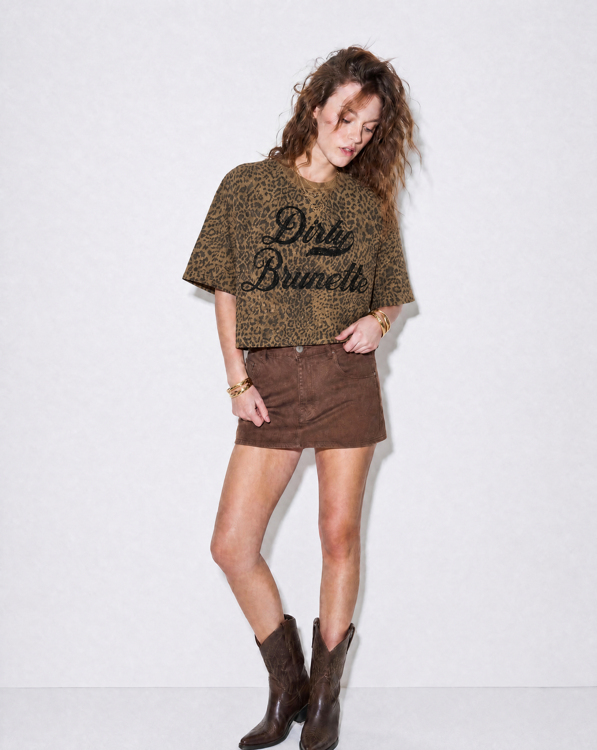 model wears a brown boxy T-shirt with an all-over animal print, contrasting ribbed crew neckline, and faded black Dirty Brunette Milkstore script graphic across the front.