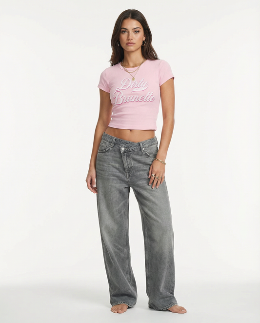 model wears a Light pink short-sleeve crop T-shirt with large cursive “Dirty Brunette” Milkstore text in white and pink on the front