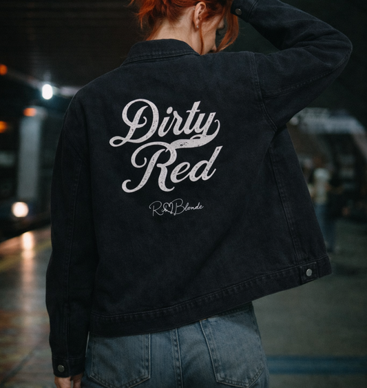 model wears a washed-black denim jacket showing large white embroidered Miklstore font script reading "Dirty Red" with the RedBlonde signature below. The jacket has a relaxed, slightly cropped silhouette and long sleeves with button cuffs.