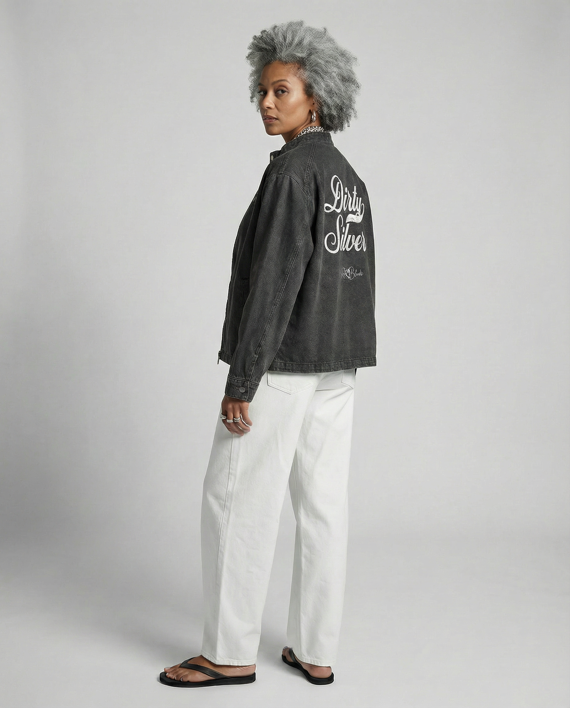 Model wears a washed-black denim jacket showing large white embroidered Miklstore font script reading "Dirty Silver" with the RedBlonde signature below. The jacket has a relaxed, slightly cropped silhouette and long sleeves with button cuffs.