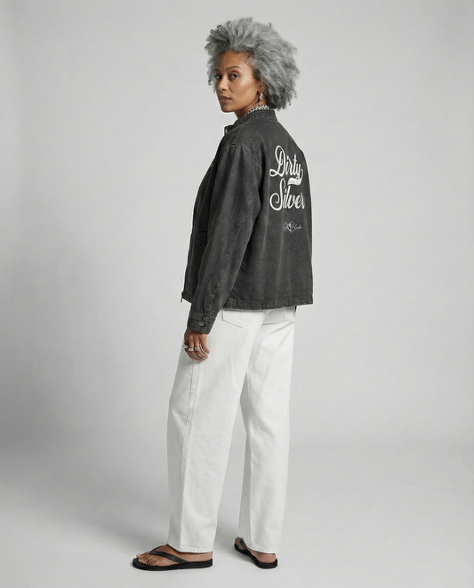 Model wears a washed-black denim jacket showing large white embroidered Miklstore font script reading "Dirty Silver" with the RedBlonde signature below. The jacket has a relaxed, slightly cropped silhouette and long sleeves with button cuffs.
