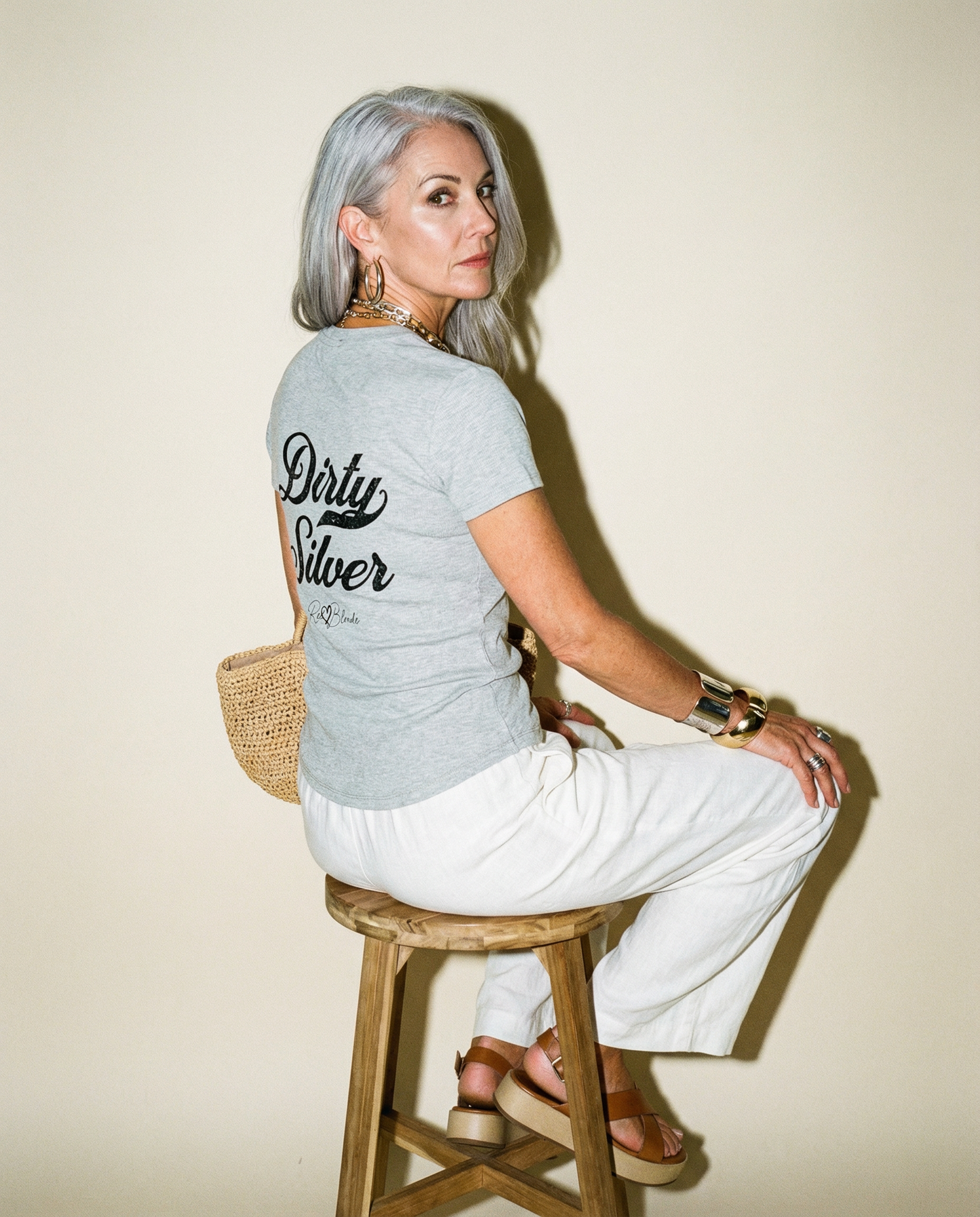Model wears a fitted, short-sleeve grey henely T-shirt featuring large black Milkstore 01 script text reading “Dirty Silver” across the upper back, with a small cursive “RedBlonde” logo beneath. The hem is slightly curved.