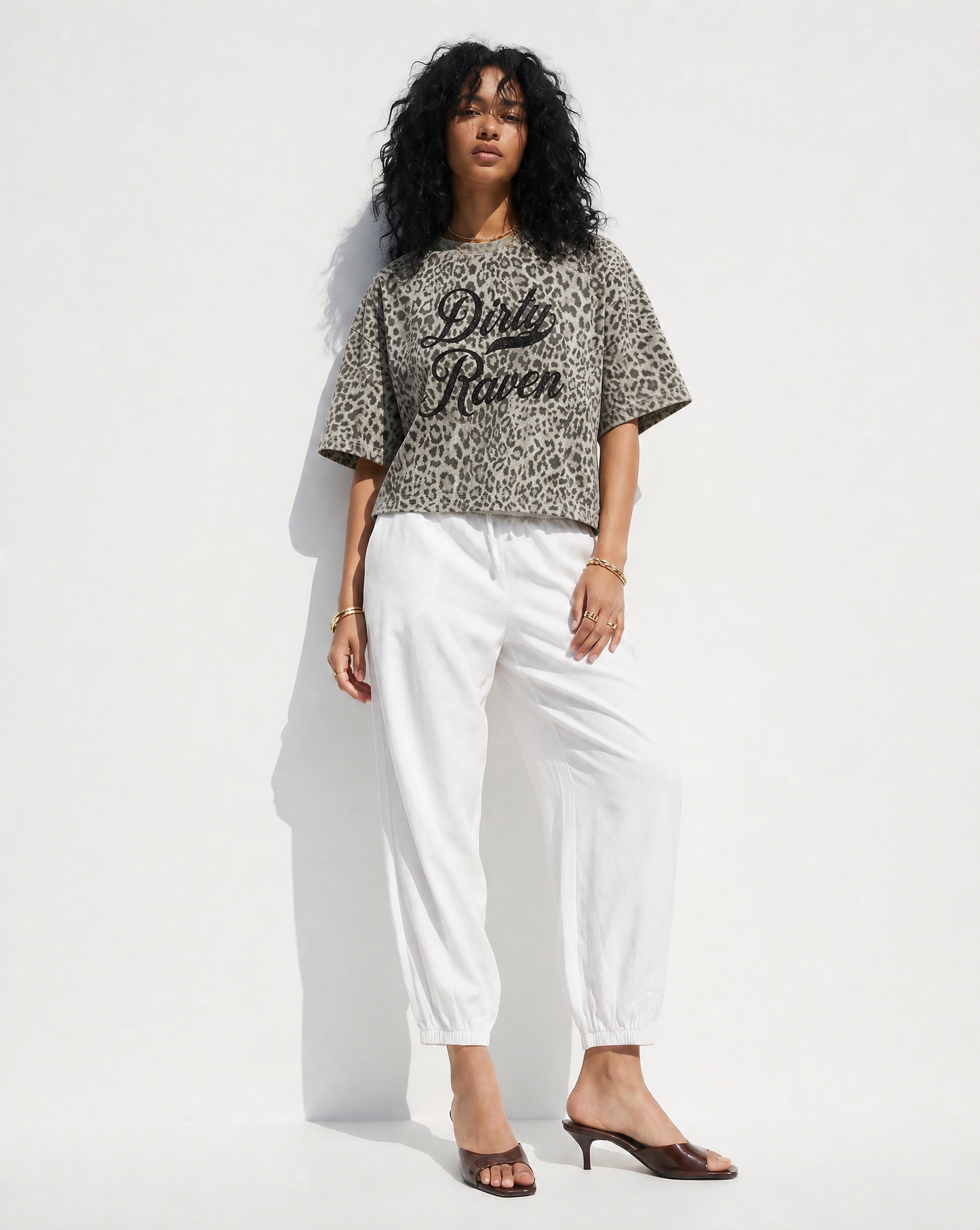 model wears a grey boxy T-shirt with an all-over animal print, contrasting ribbed crew neckline, and faded black Dirty Raven Milkstore script graphic across the front.