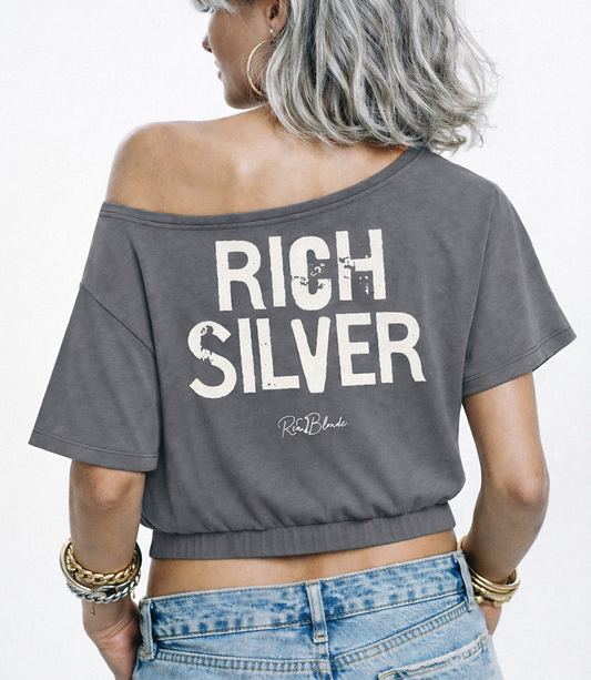 model wears a grey asymmetrical shoulder t-shirt with bold white Ed Gein font “RICH SILVER" slogan on the front and RedBlonde logo beneath.