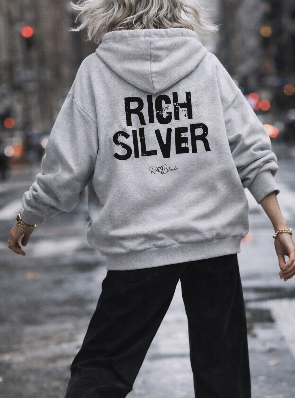 model wears a grey hem to hood zip-up hoodie with cropped oversized fit and ribbed cuffs/hem, featuring large distressed black “RICH SILVER” Ed Gein text across the back with a small “RedBlonde” script logo beneath.