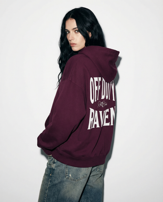 model wears a plum oversized hoodie shown from the back  featuring large white “OFF DUTY RAVEN” Brookfield text with a small RedBlonde script logo between the words.