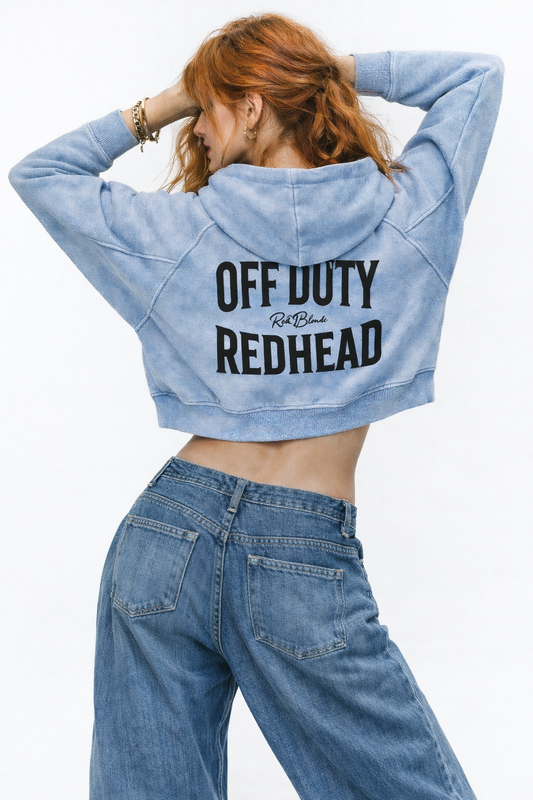 model wears a soft blue cropped hoodie with a hood and long sleeves, featuring large black ‘OFF DUTY REDHEAD' text and a small RedBlonde logo on the back.”