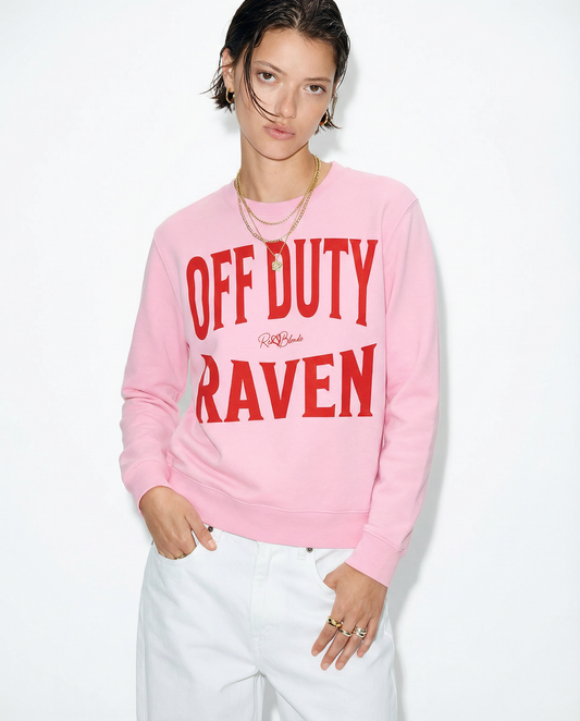 model wears pink crewneck sweatshirt with a large red “OFF DUTY RAVEN” graphic across the chest and a small RedBlonde script logo centered between the words.