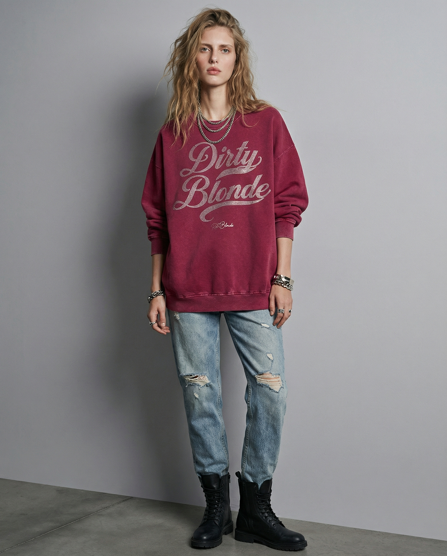 Model wears Red snow-wash oversized sweatshirt with a drop-shoulder fit, featuring a rhinestone-style “Dirty Blonde” Milkstore script graphic across the front and a small RedBlonde logo near the hem.