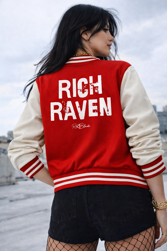 model wears red & white varsity-style jacket with cream sleeves and striped ribbed trims. The back features large white text reading “RICH RAVEN” in Ed Gein font with a small RedBlonde signature logo in the centre between the words