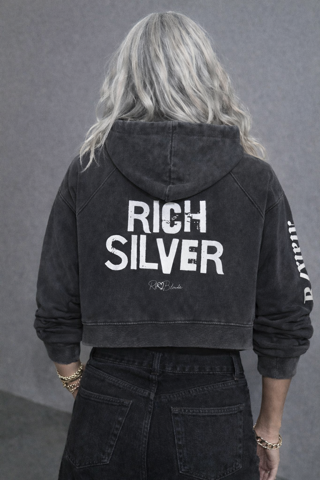 model wears a cropped snow-wash black  hoodie with bold black “RICH SILVER” Ed Gein font and the RedBlonde signature logo printed below.