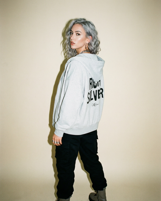 model wears a grey hem to hood zip-up hoodie with cropped oversized fit and ribbed cuffs/hem, featuring large distressed black “RICH SILVER” Ed Gein text across the back with a small “RedBlonde” script logo beneath.