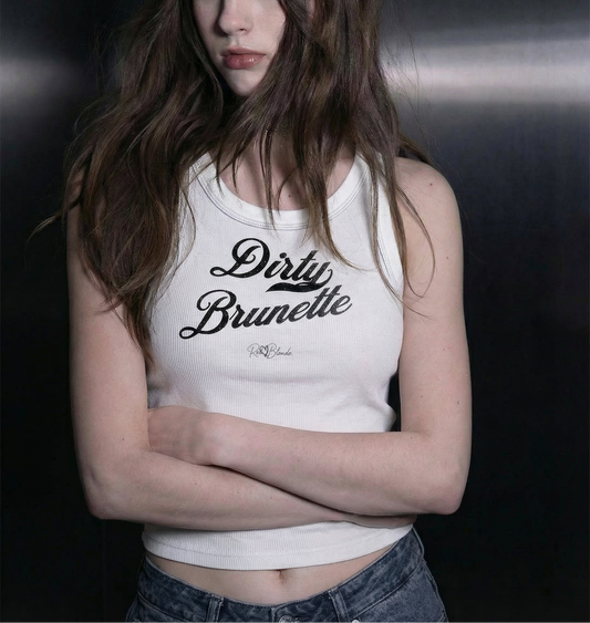 Brunette wears a white snow-wash tank top with raw-edge seams and the phrase ‘Dirty Brunette’ printed in vintage Milkstore black font across the chest, featuring the RedBlonde logo underneath