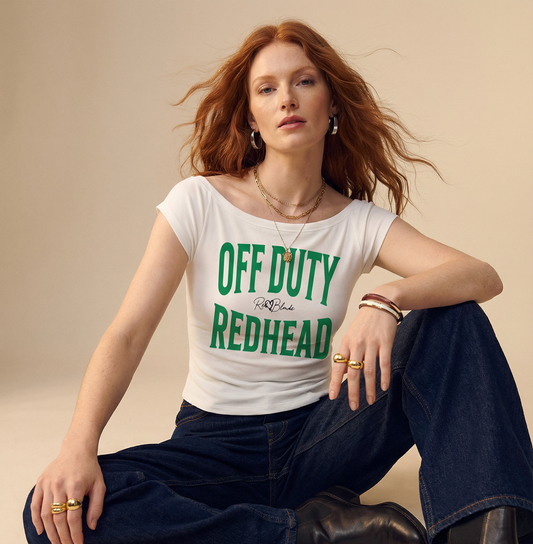 model wears a white raglan short-sleeve top with bold green Brookfield lettering reading “OFF DUTY REDHEAD” with a small cursive RedBlonde logo between the words