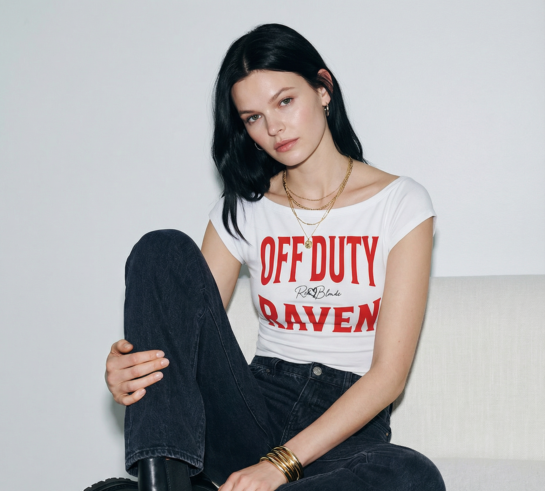 model wears a White raglan short-sleeve top with bold red Brookfield lettering reading “OFF DUTY RAVEN” with a small cursive RedBlonde logo between the words