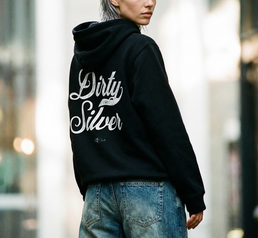 Silver haired model wears a black hoodie with bold black Milkstore vintage-style script text “Dirty Silver” across the back and a subtle RedBlonde signature logo underneath