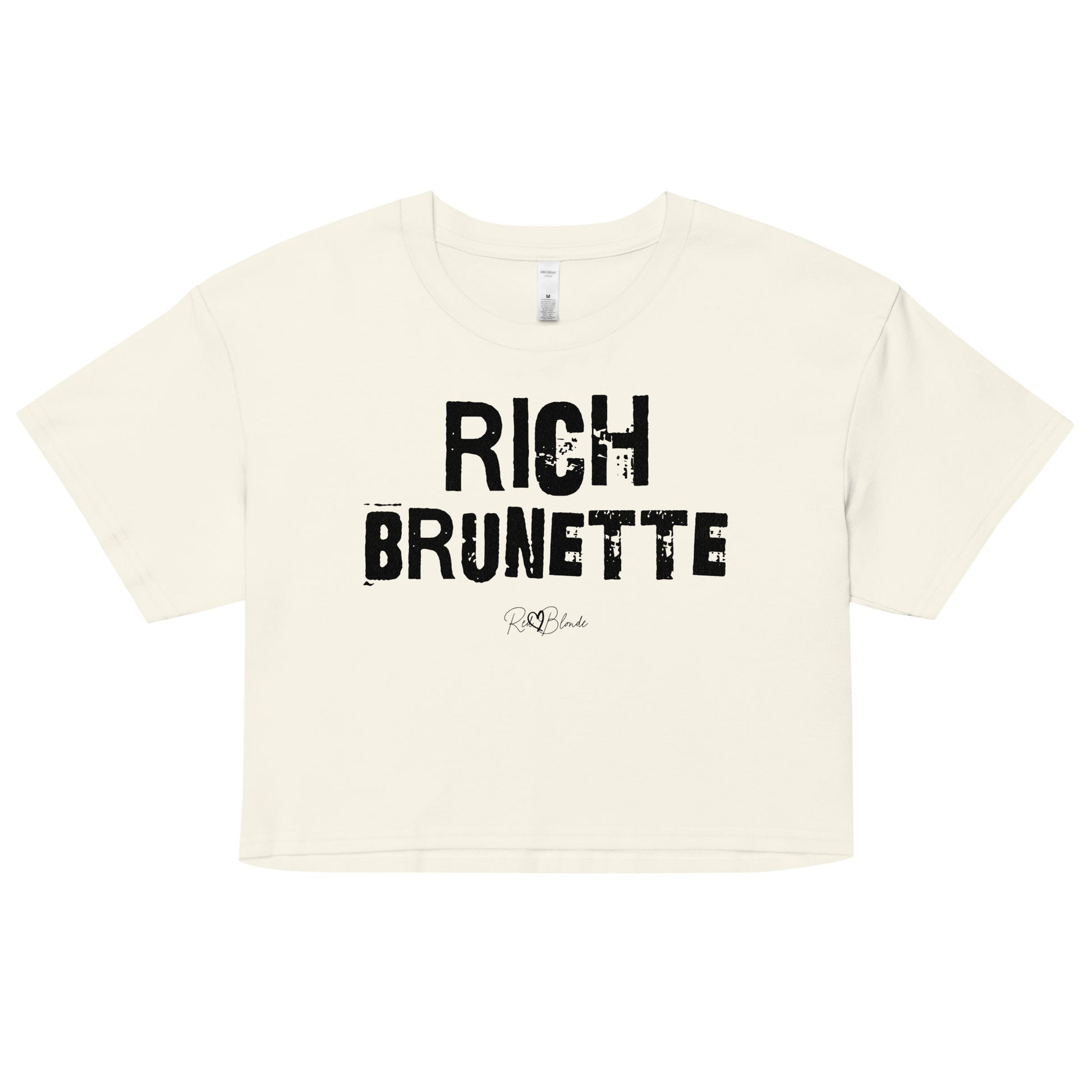 a natural coloured crop top with a relaxed fit, short sleeves, and a wide crew neckline. The front features bold black distressed Ed Gein lettering reading “RICH BRUNETTE” with the RedBlonde signature logo underneath in black