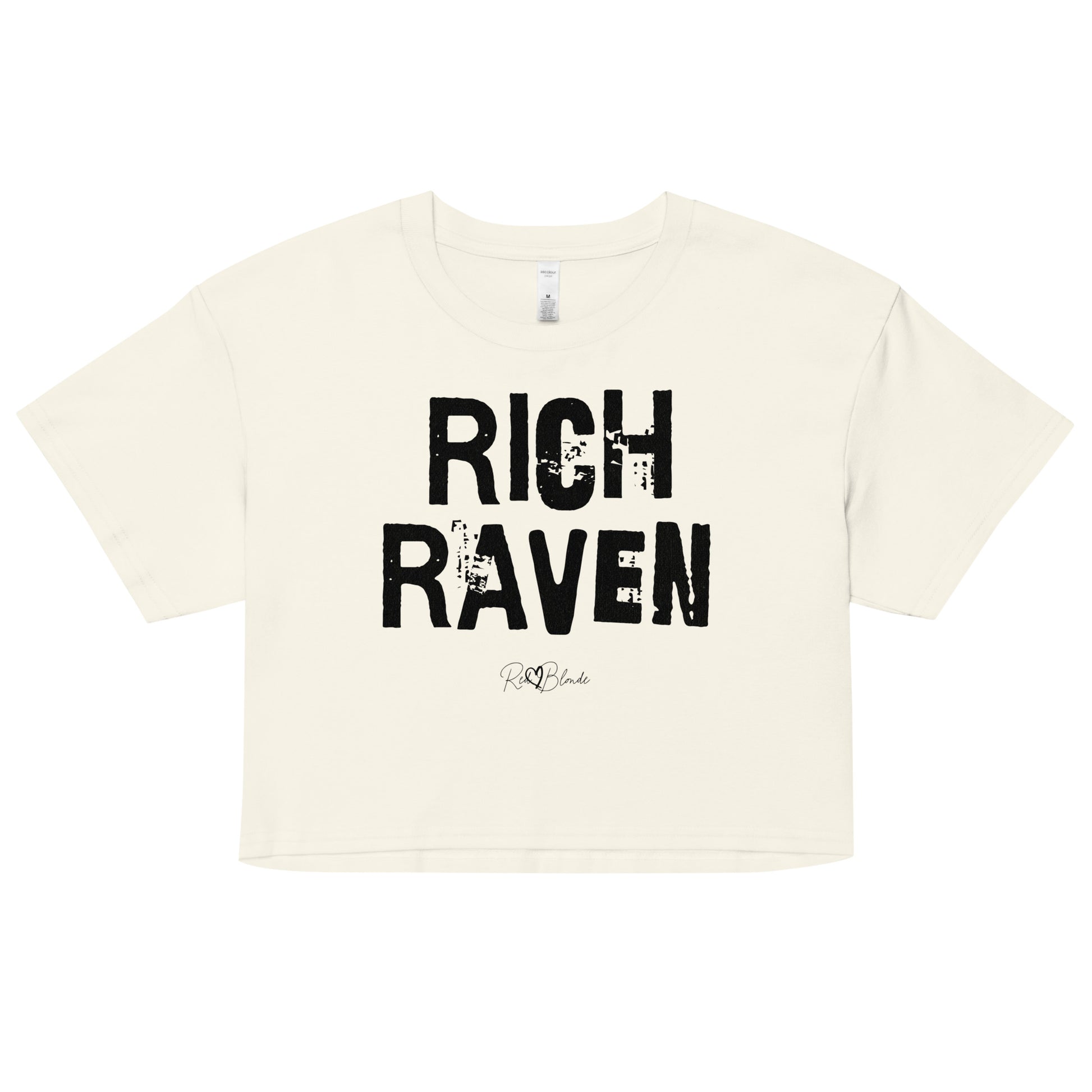 A natural coloured crop top with a relaxed fit, short sleeves, and a wide crew neckline. The front features bold black distressed lettering reading “RICH RAVEN” with the RedBlonde signature logo underneath in black