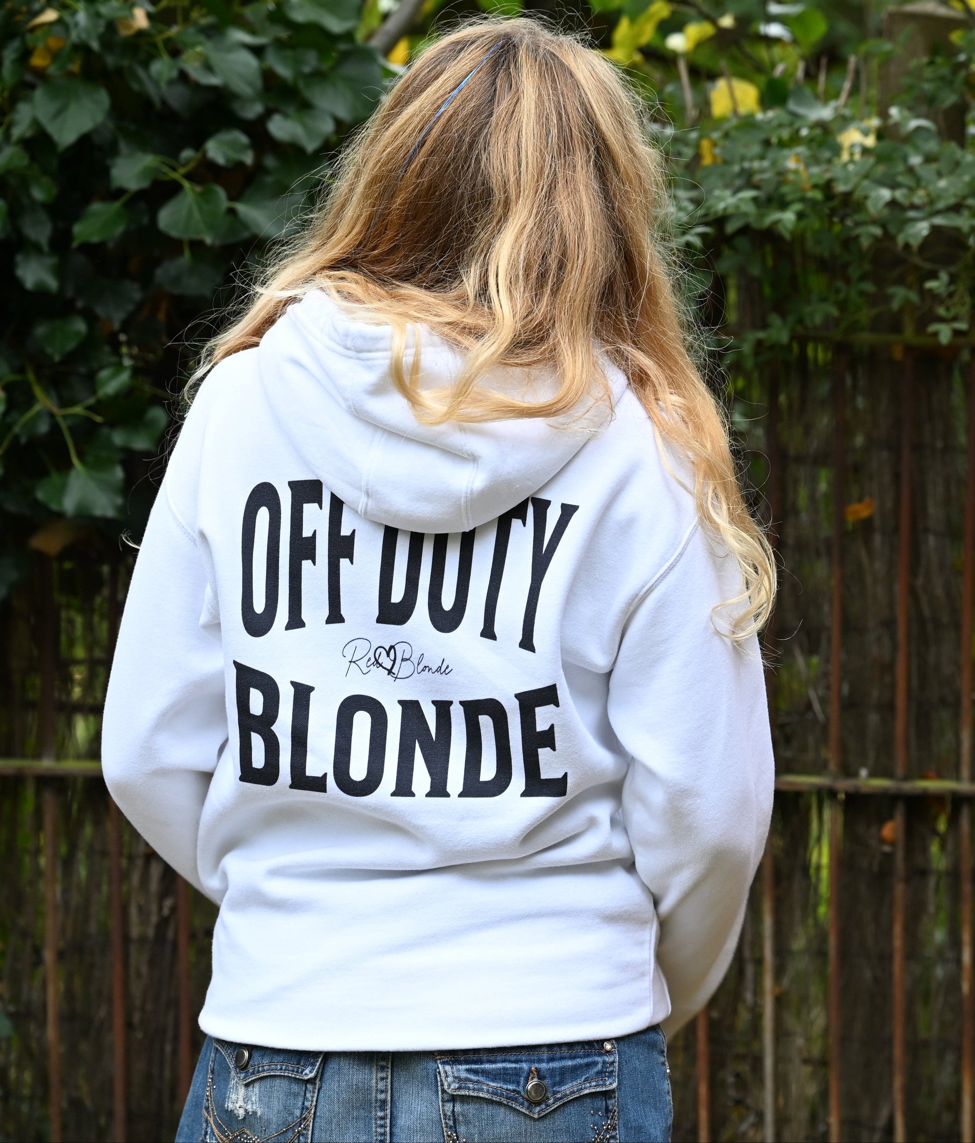 Blonde wears a classic black unisex hoodie with the words 'OFF DUTY BLONDE' written in large Brookfield white font, across the back. Branded RedBlonde London in red on inside neck and right sleeve 
