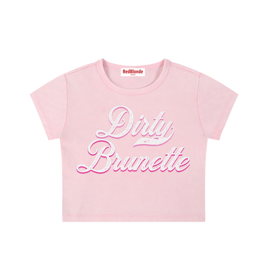 Light pink short-sleeve crop T-shirt with large cursive “Dirty Brunette” Milkstore text in white and pink on the front, and a small “RedBlonde London” label at the neckline.