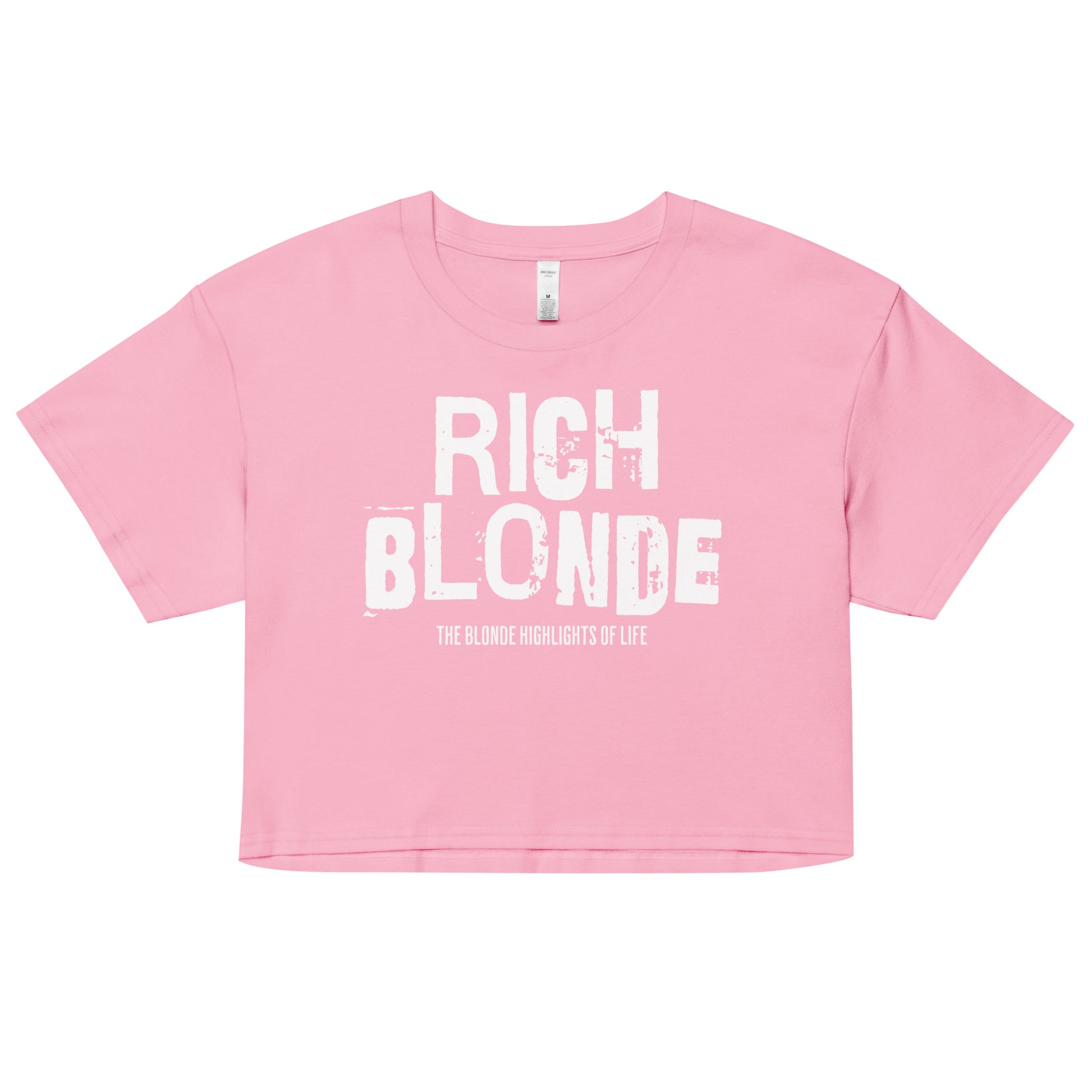 A pink women’s crop top with a relaxed fit, short sleeves, and a wide crew neckline. The front features bold white distressed lettering reading “RICH BLONDE” with the tagline “THE BLONDE HIGHLIGHTS OF LIFE” in smaller text below. 