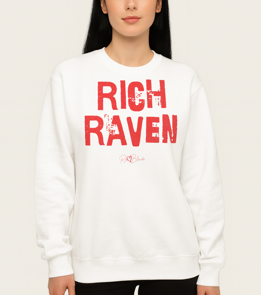 Model with jet black hair wears a White unisex premium sweatshirt with bold distressed Red Ed Geinitext “RICH RAVEN” on the front, featuring a subtle RedBlonde logo beneath the lettering and on the sleeve cuff and inside neck