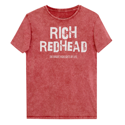 A red acid-wash unisex denim T-shirt with a distressed vintage look. The shirt features the bold white text “RICH REDHEAD” in a weathered Ed Gein font, with the tagline “THE BLONDE HIGHLIGHTS OF LIFE” in smaller uppercase letters below. The shirt has short sleeves, a crew neckline, and visible seam detailing for a rugged, casual style. Branded Redblonde on inside neck and right sleeve