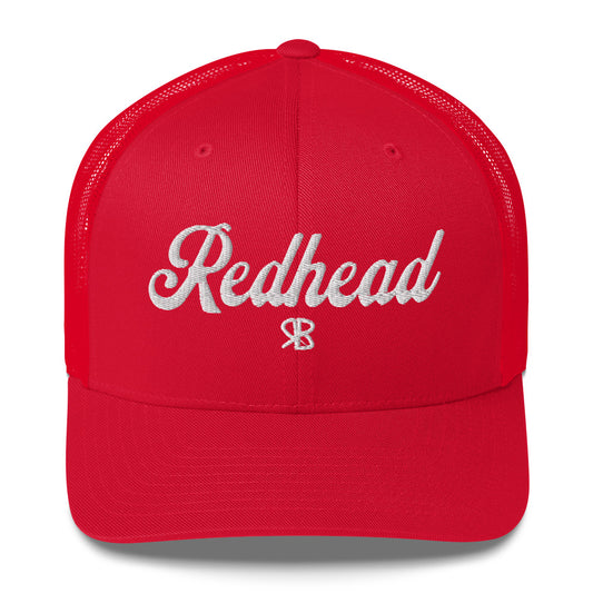 red trucker cap with 'Redhead' in white adventurer 01 font on front. Mesh back. Branded RB