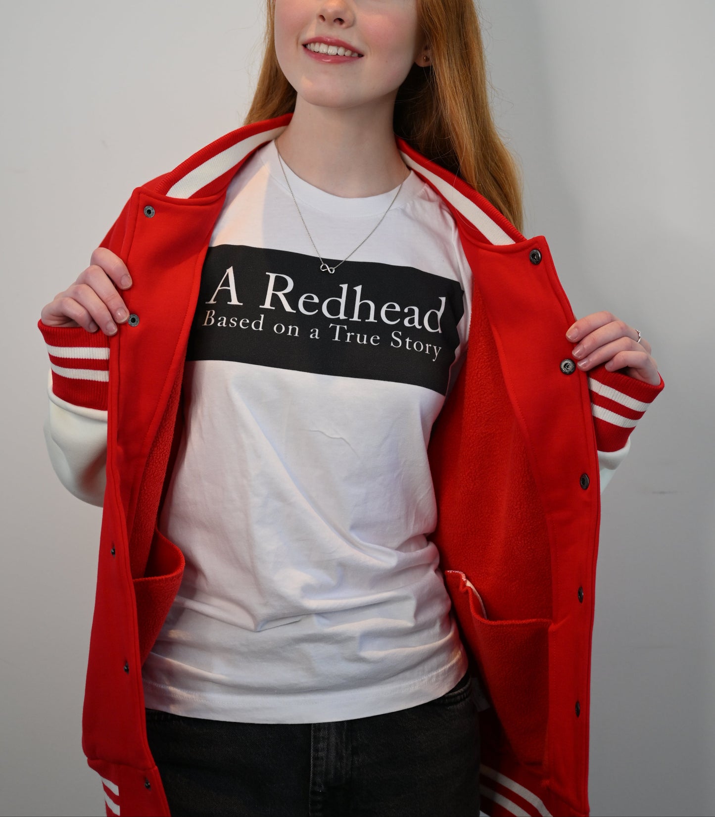 redhead model, by stone steps, wears a white unisex relaxed fit t-shirt with the slogan 'A Redhead. Based on a True Story' in white text in a black box graphic 