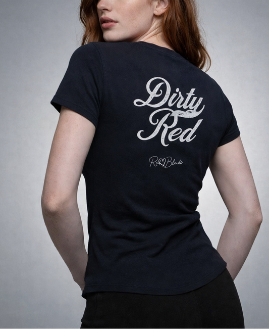 Redhead wears a fitted, short-sleeve black T-shirt laid flat on a white background. It features large black Milkstore 01 script text reading “Dirty Red” across the upper back, with a small cursive “RedBlonde” logo beneath. The hem is slightly curved.