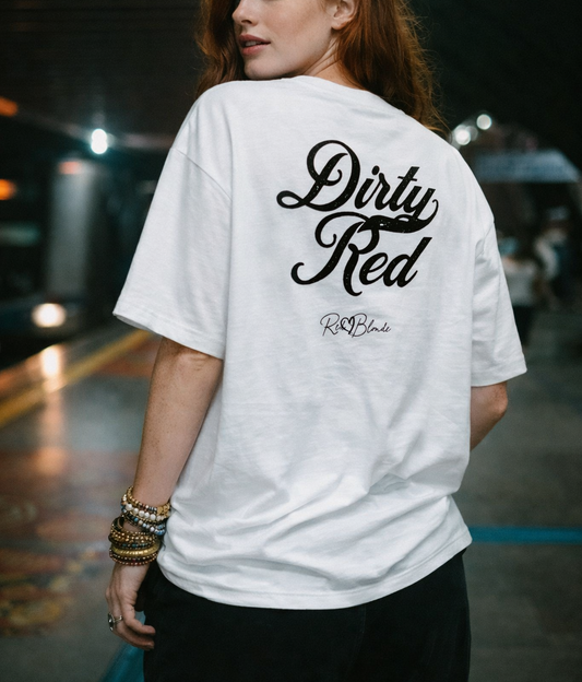 Redhead wears a of a white oversized boxy short-sleeve T-shirt laid flat on a white background. Large distressed black Milkstore 01 script text reads “Dirty Red,” with a small cursive “RedBlonde” logo beneath the main graphic.