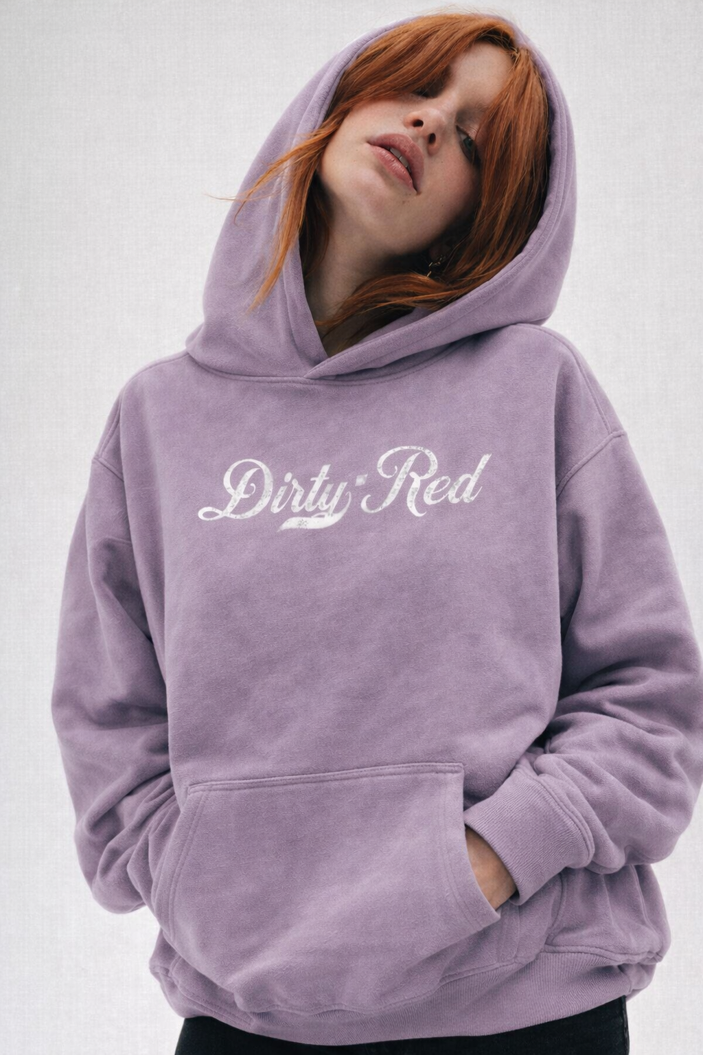 Redhead wears a A lavender pullover hoodie laid flat on a white background. It has a kangaroo front pocket and ribbed cuffs and hem. Across the chest is white Milkstore 01 script text reading “Dirty Red.”