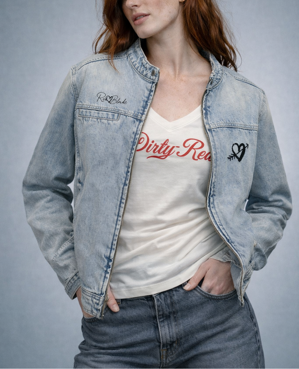 redhead wears a redblonde denim jacke and a white V-neck T-shirt laid flat on a white background. It has short sleeves and a red Milkstore 01 script graphic across the chest reading “Dirty-Blonde.” A small RedBlonde label is visible at the inside back neck.