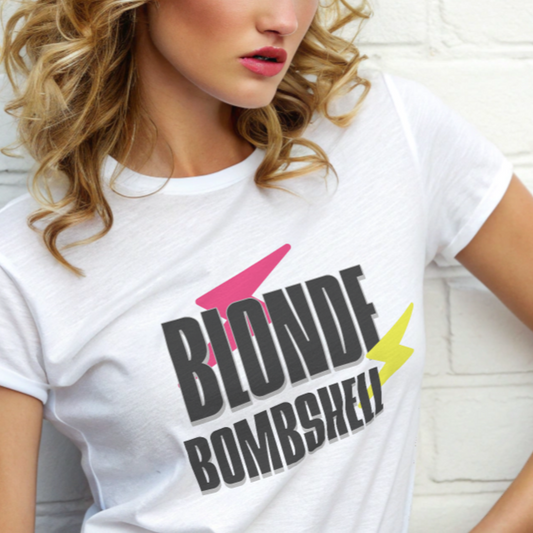Blonde model by a wall wears a relaxed-fit white t-shirt with bold 80s ‘David Bowie’ inspired lightning graphic flashes of pink and yellow around the words ‘blonde bombshell’.