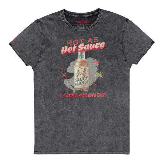 flatlay of a relaxed dark grey denim-wash t-shirt with a retro American-vintage pop-art graphic featuring a bottle of sauce with Saucy Blonde on it and the words Hot As hot Sauce. branded with redblonde london in red on the inside neck and right shoulder
