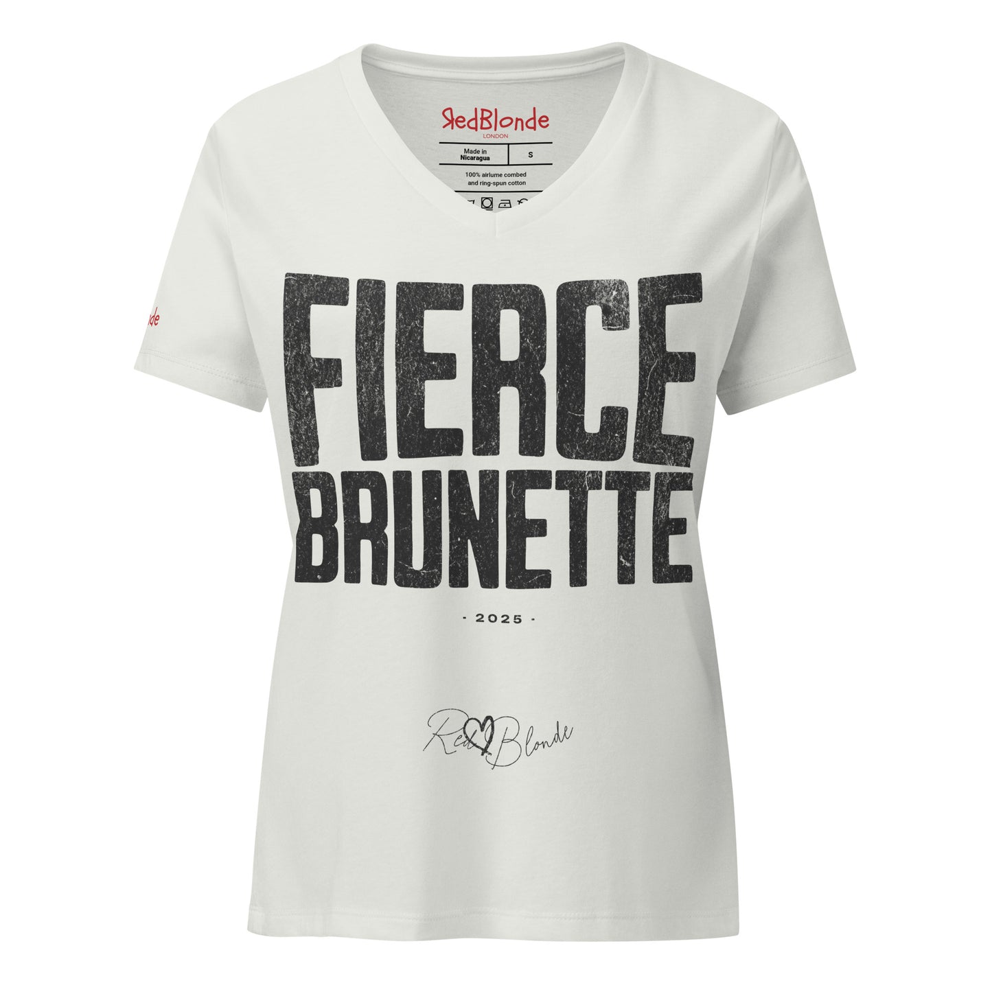silver women’s V-neck T-shirt featuring the bold black distressed text “FIERCE BRUNETTE” in large North Road capital letters across the chest. Beneath the text, the year “2025” is printed in small type, with the “RedBlonde” brand signature logo below it. The inner collar shows the “RedBlonde” brand name in red along with sizing and care details, and “RedBlonde” is also printed in small red letters on the right sleeve.