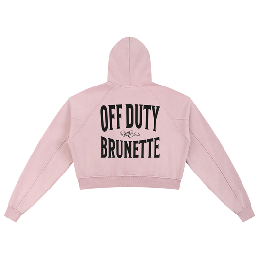 “Back view of a soft pink cropped hoodie with a hood and long sleeves, featuring large black ‘OFF DUTY BRUNETTE' text and a small RedBlonde logo on the back.”