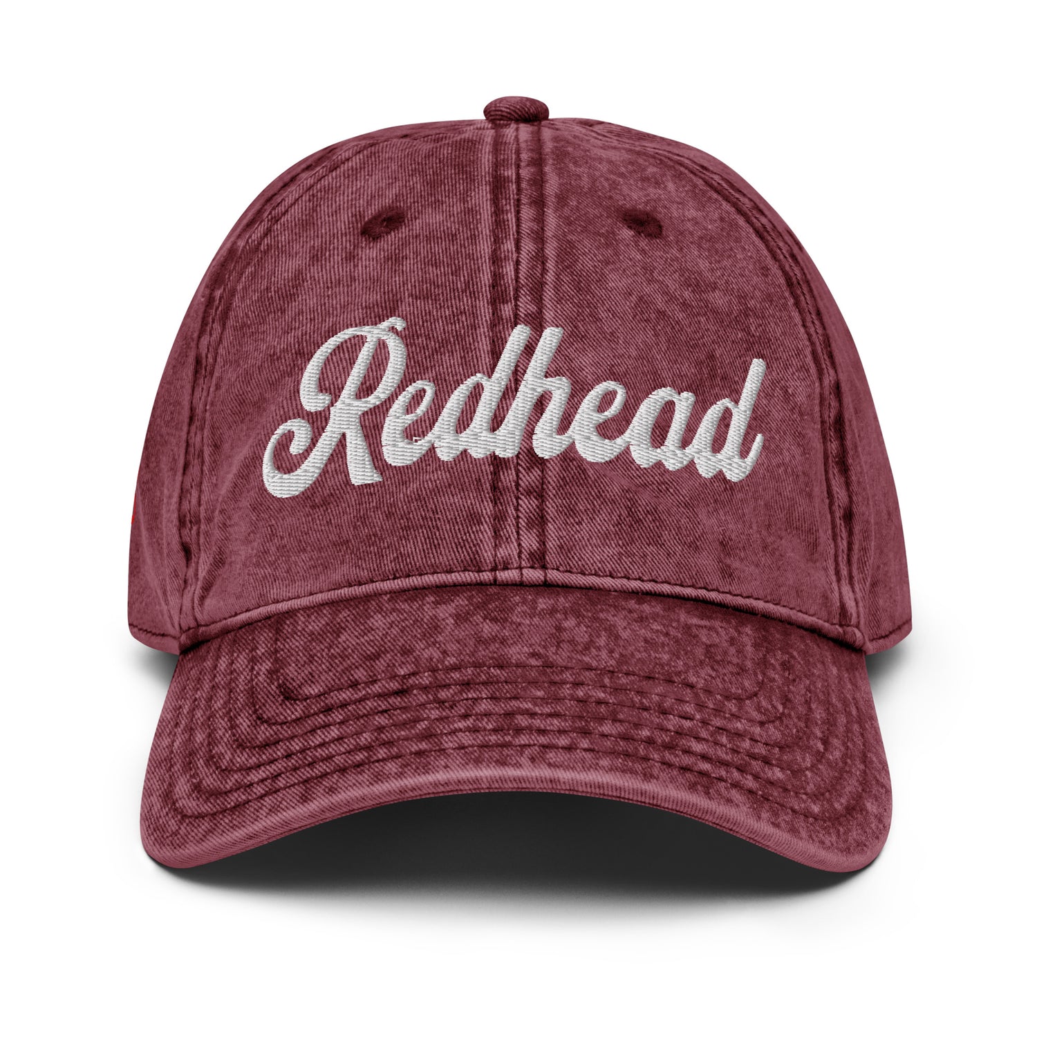 flatlay of vintage maroon denim wash effect baseball cap with the word 'Redhead' embroidered on the front in white adventure type script font 