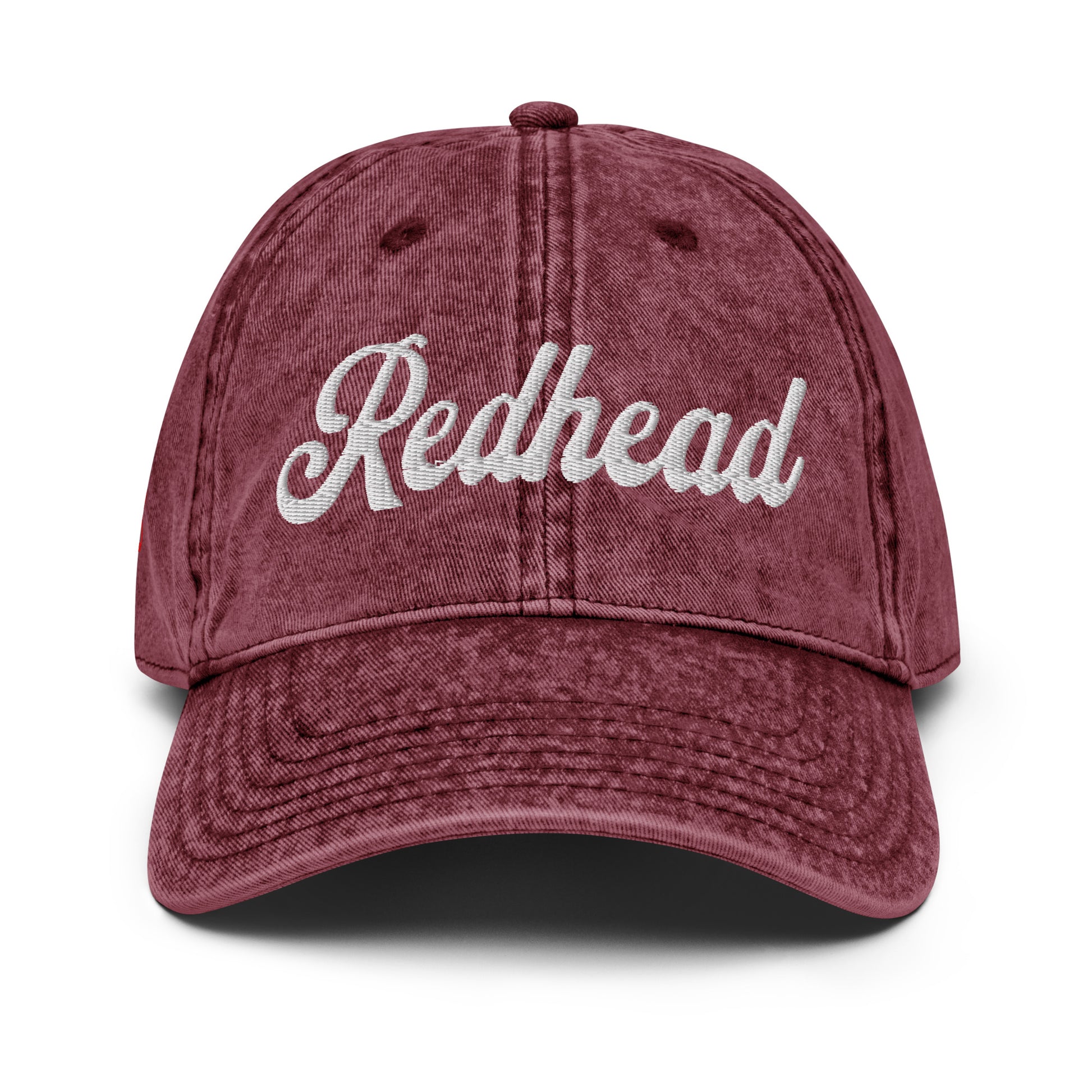 flatlay of vintage maroon denim wash effect baseball cap with the word 'Redhead' embroidered on the front in white adventure type script font 