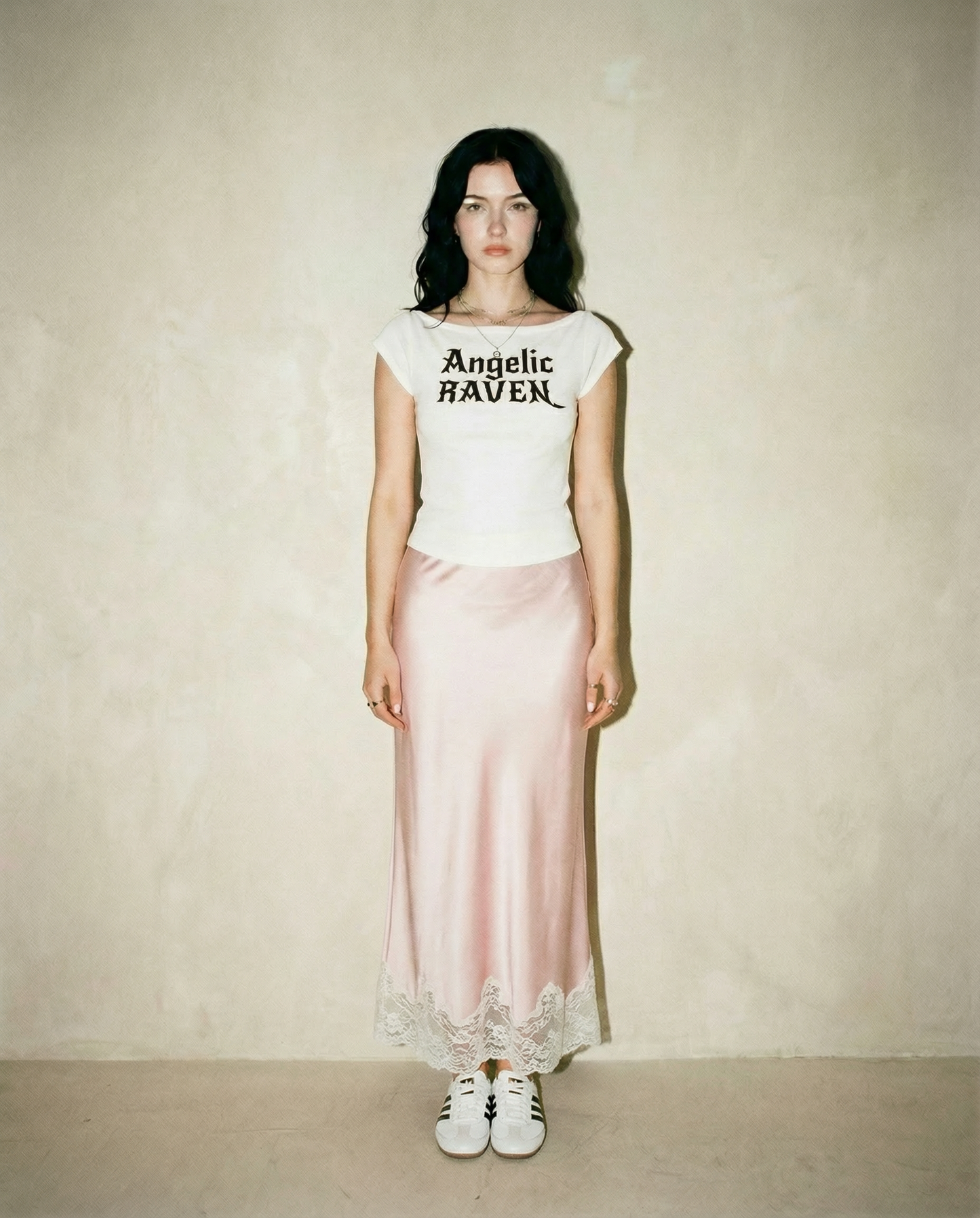white wide-neck t-shirt with white gothic New Rockstar text reading “Angelic Raven” across the chest.