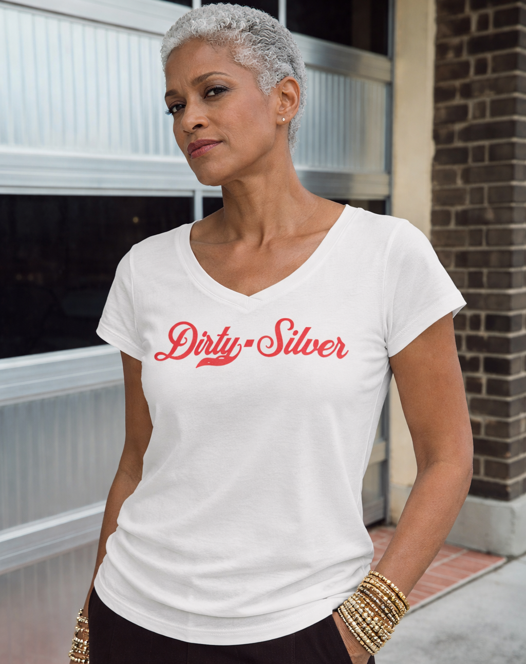 model wears white V-neck T-shirt laid flat on a white background. It has short sleeves and a red Milkstore 01 script graphic across the chest reading “Dirty-Silver.” A small RedBlonde label is visible at the inside back neck.