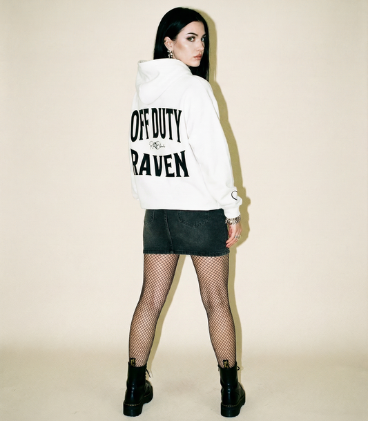 model wears white hoodie, back view, with large black  ‘OFF DUTY RAVEN’ Brookfield text print and small RedBlonde signature logo beneath. Black heart detail on the sleeve