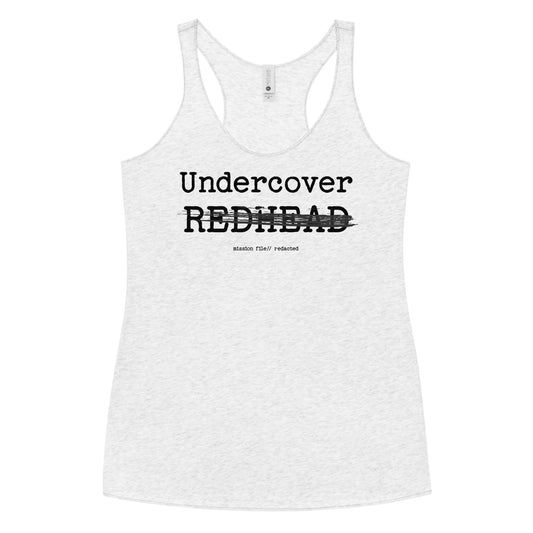 A white racerback tank featuring a bold black text reading “Undercover REDHEAD” with “REDHEAD” partially struck through by a horizontal black bar. Beneath it, smaller text says “mission file // redacted” along with a subtle RedBlonde logo. Branded RedBlonde London in red on the reverse